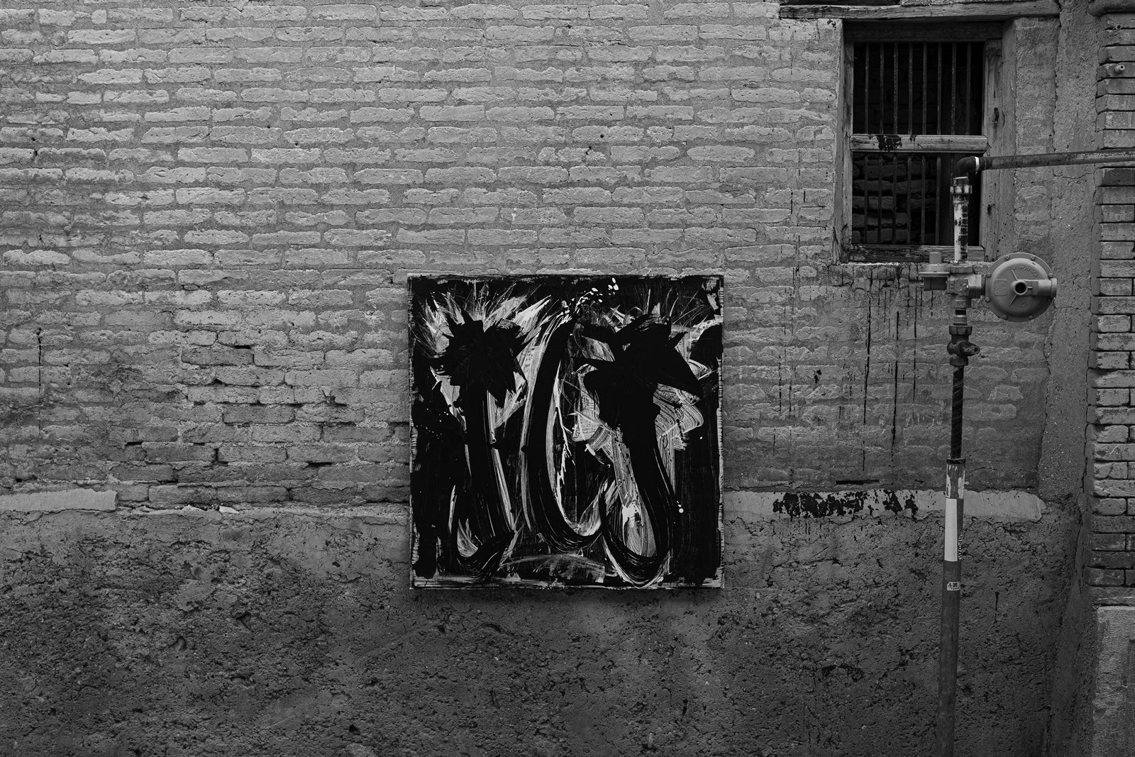 A dark canvas on a mud-brick wall beside a gas pipe